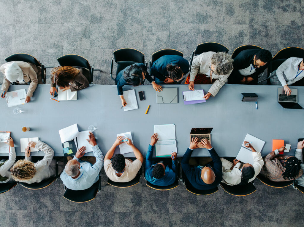 Overhead perspective of a meeting room with attendees seated around a table, collaborating on ideas.